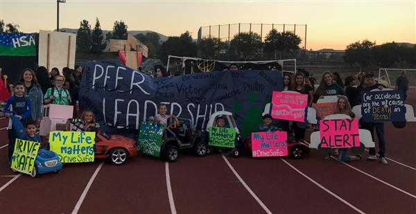Several high school students stand behind toy cars with signs posted on them. Small kids sit in the cars.n toy car Several high school students stand behind toy cars with signs posted on them. Small kids sit in the cars.n toy car